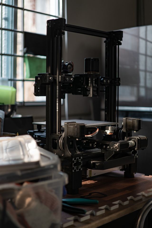 A detailed view of a 3D printer in a workshop with ambient light.